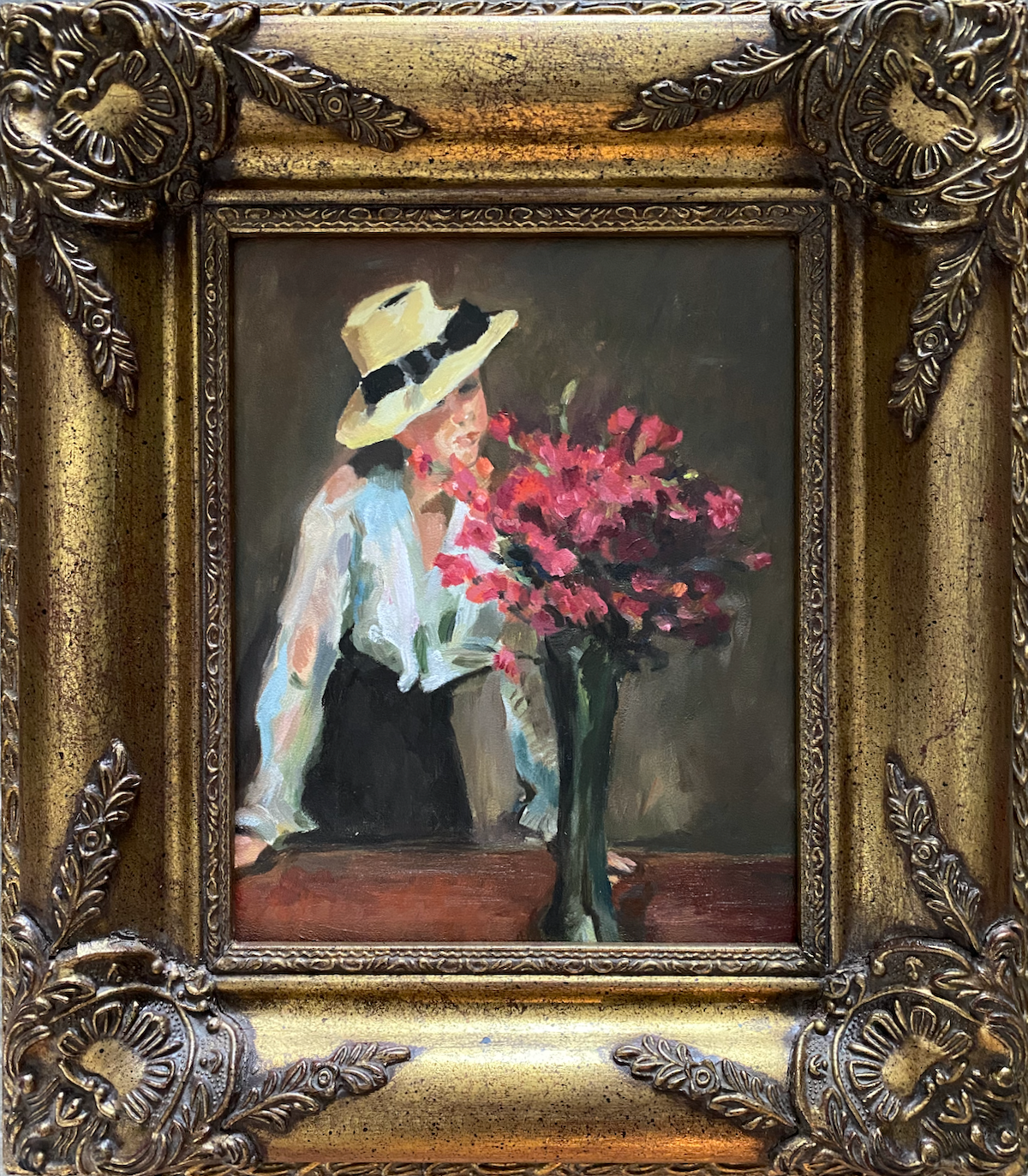 vrouw met hoed, witte blouse en donkere rok staand achter een grote vaas met rode bloemen